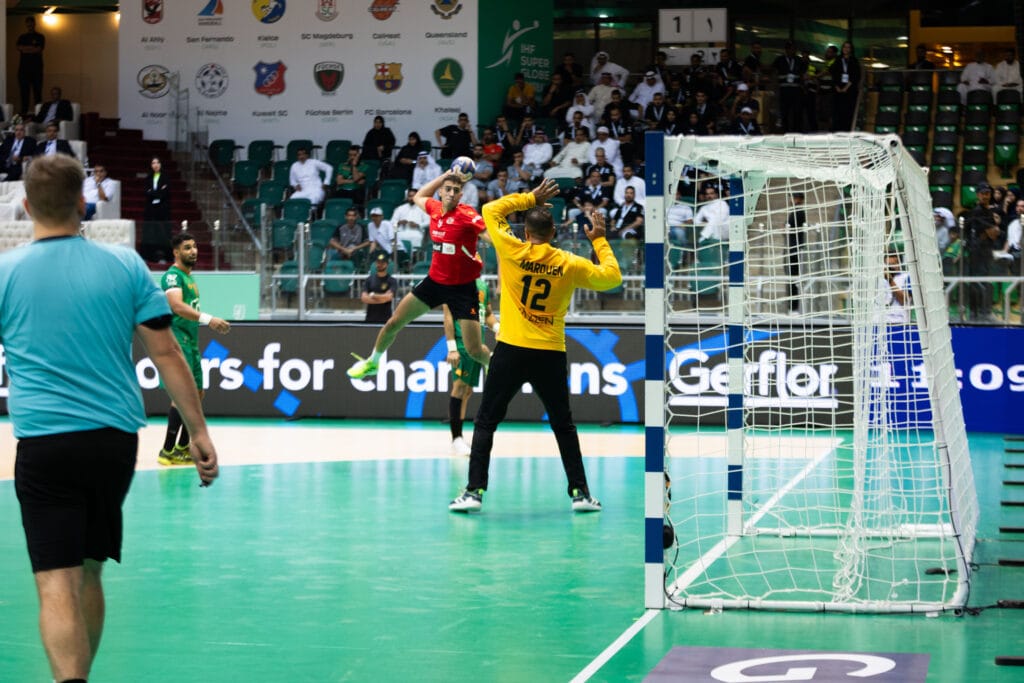 Handball player leaps, scoring goal.