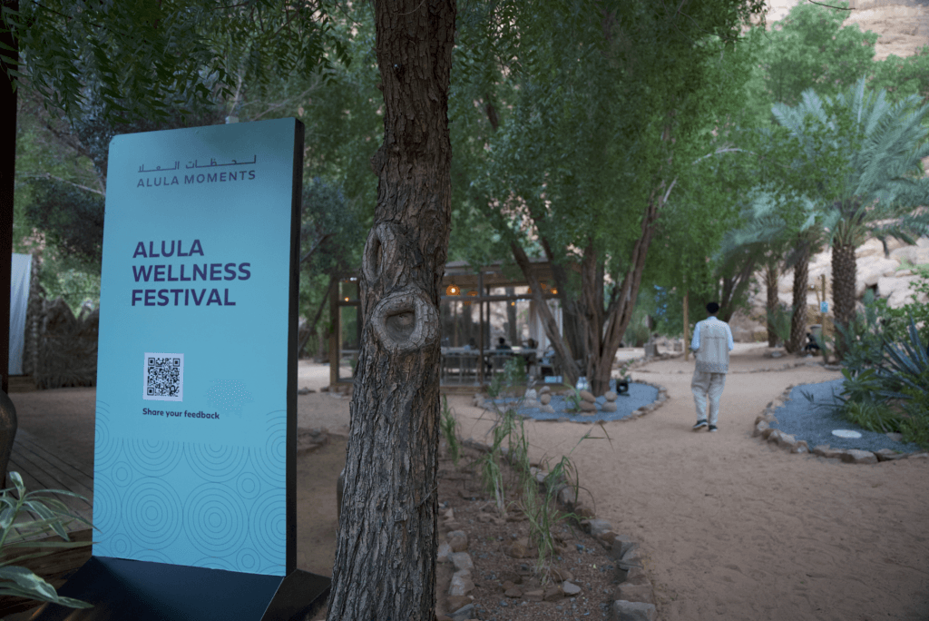 A sign for the Alula Wellness Festival surrounded by greenery, showcasing image.