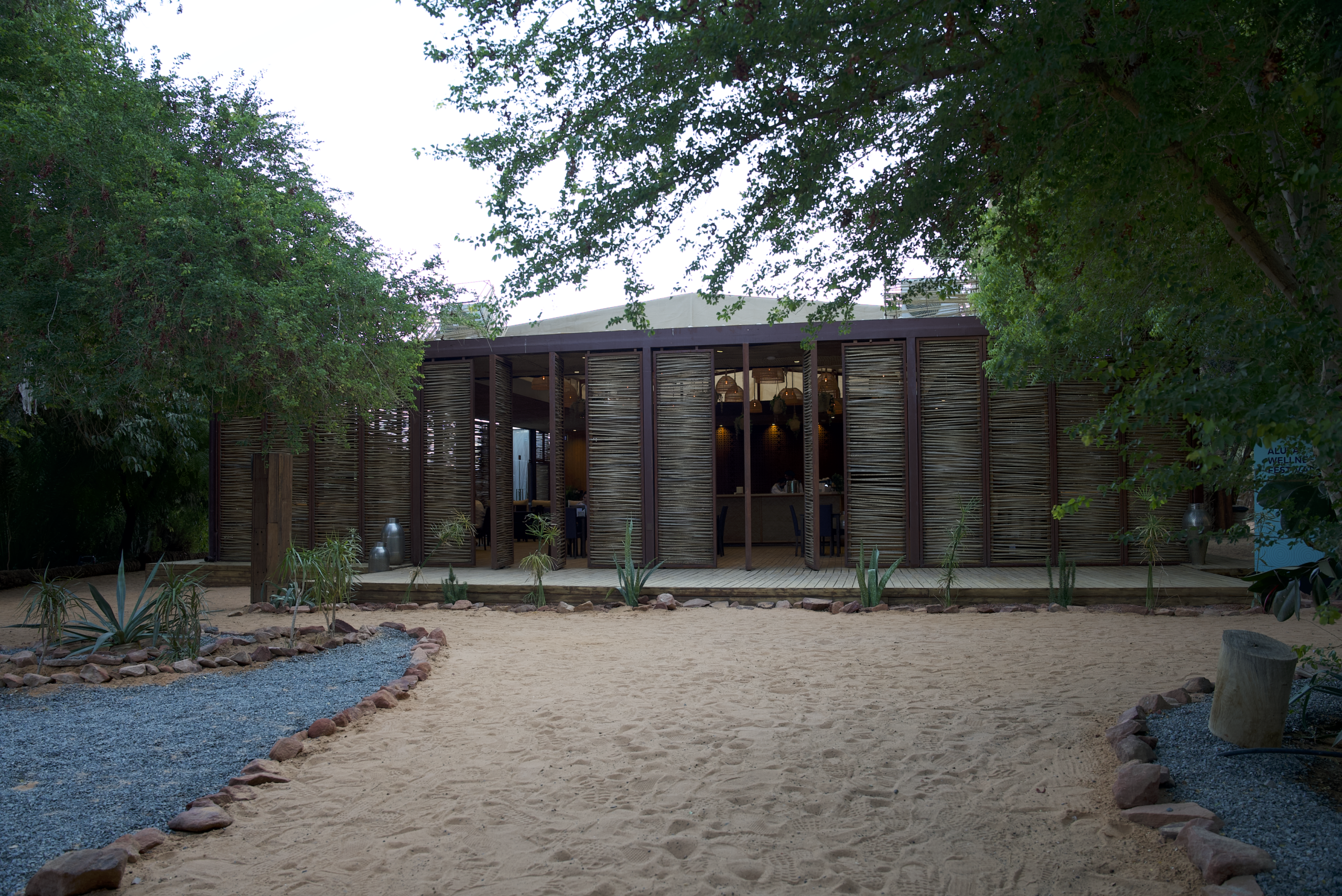 A modern wooden house surrounded by lush greenery and a sandy path, showcasing image.