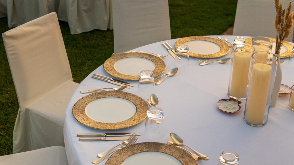 An outdoor dining setup with white tables and chairs illuminated by string lights at twilight, showcasing image.