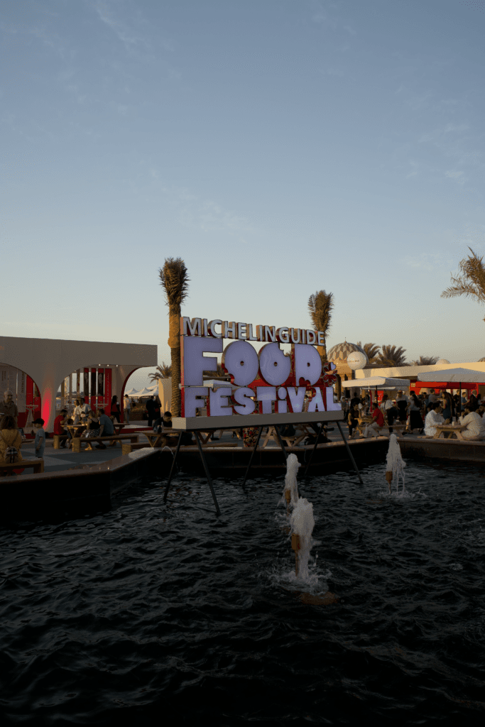 A vibrant sign for the Michelin Guide Food Festival near a water fountain, showcasing image.