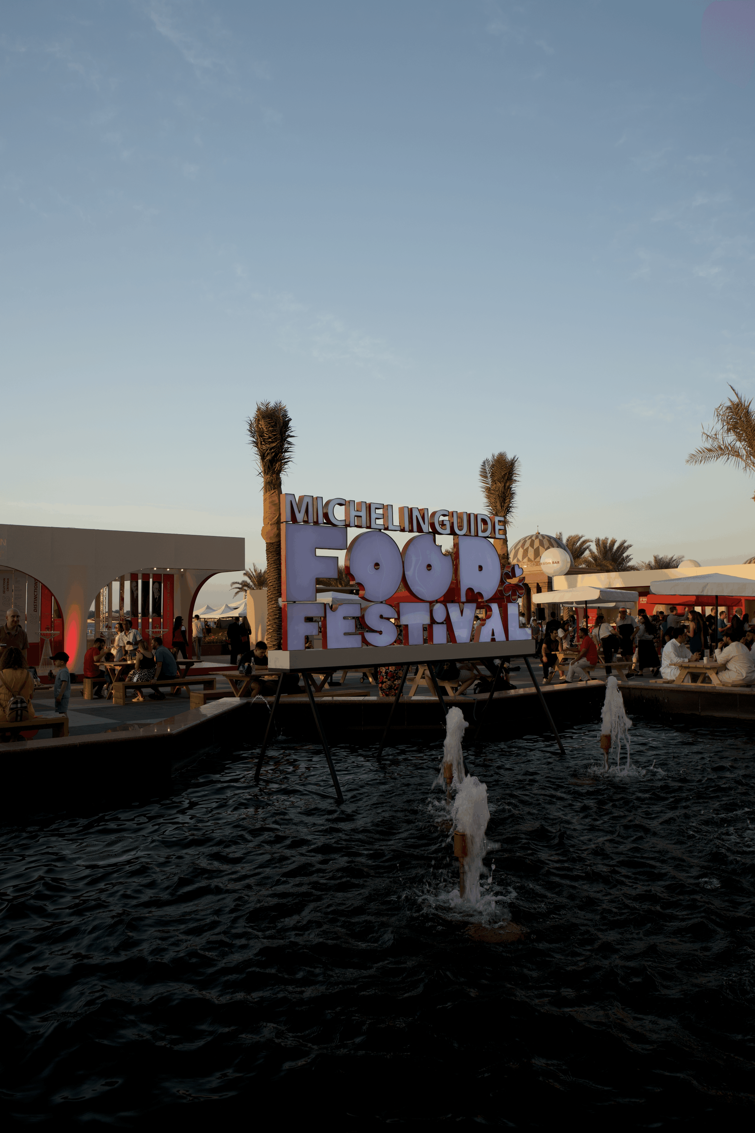 A vibrant sign for the Michelin Guide Food Festival near a water fountain, showcasing image.