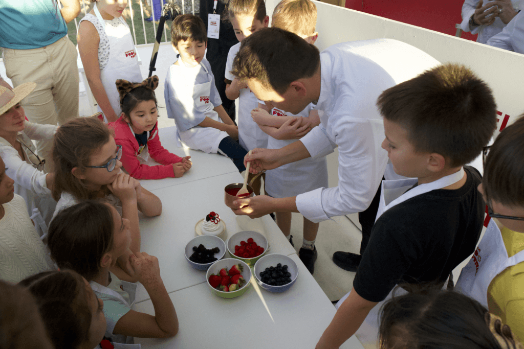 A chef demonstrating dessert preparation to children in a cooking class, showcasing image.